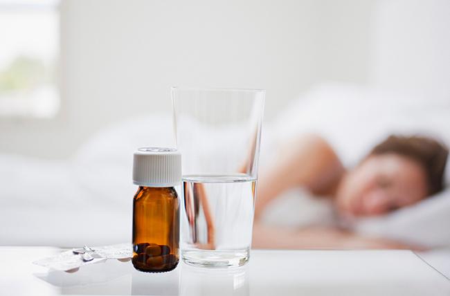 A woman is sleeping in the bed with a glass of water and pills on the nightstand.