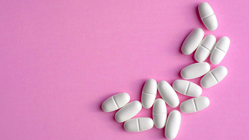 White pills arranged in a curve on a pink background.