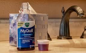 A bottle of NyQuil, a cold and flu medicine, sits on a bathroom counter next to a sink.
