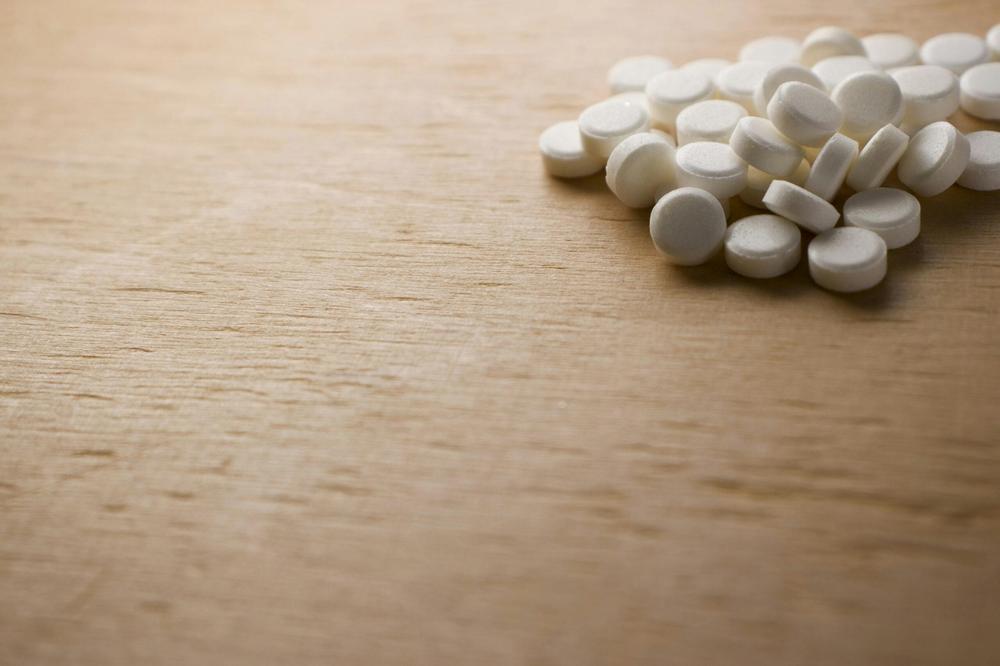 A pile of white pills on a wooden table.