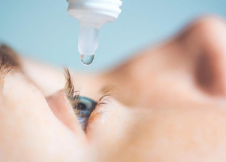 A woman is putting eye drops into her eye.