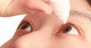 A woman is applying eye drops to her right eye.