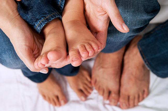 An adult is holding a babys feet in their hands while another adult is holding the babys other foot.