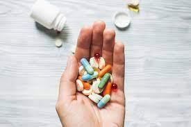 A hand holding a variety of pills and capsules.