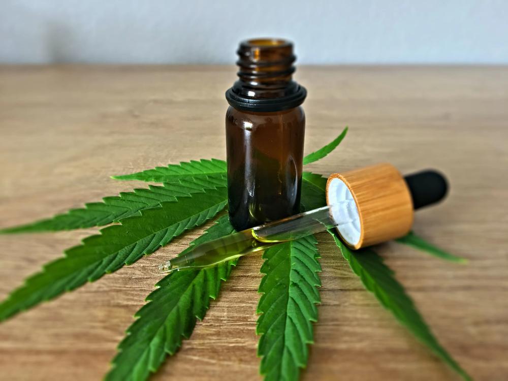 A dropper bottle of CBD oil sits on a cannabis leaf.
