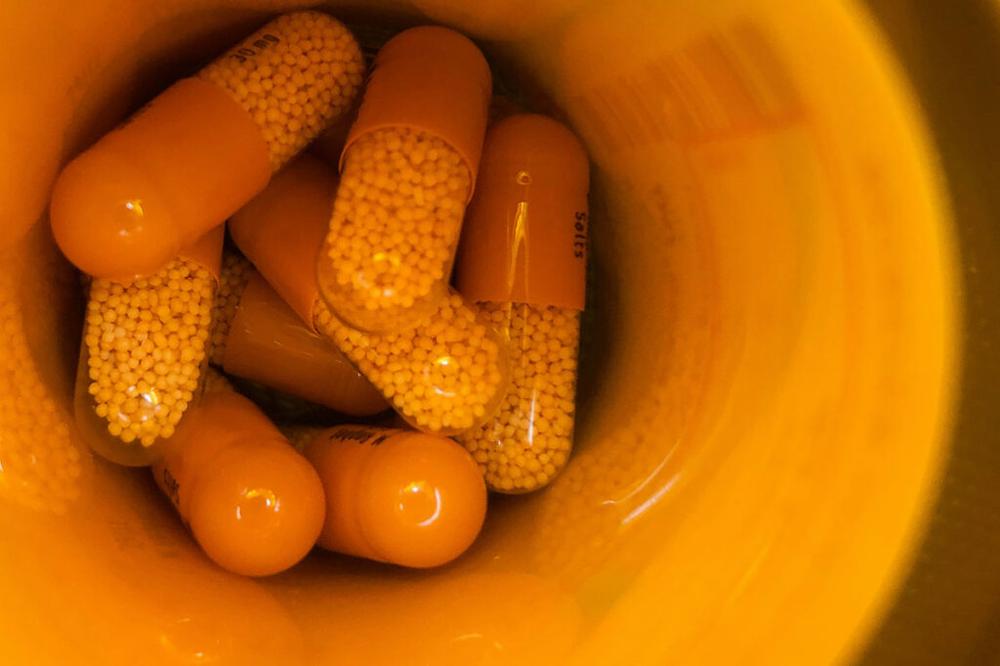 Several orange and yellow pills sit in a prescription bottle.