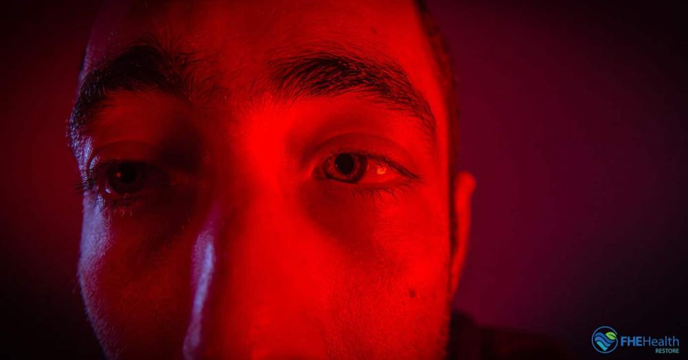 A mans face is lit up with red light.