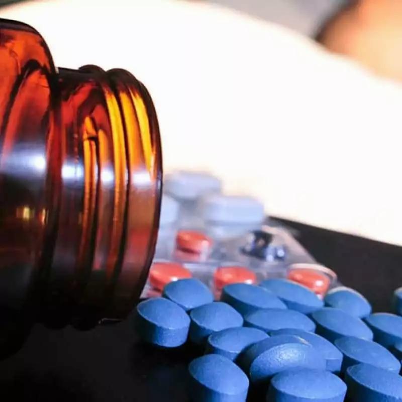 Blue pills spilled out of a brown prescription bottle.
