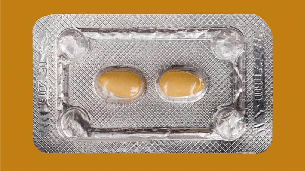 Two yellow pills in a silver blister pack on an orange background.