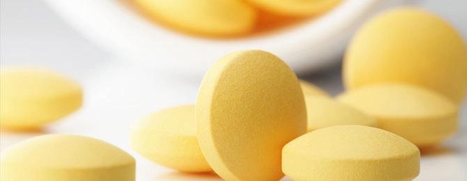 Several yellow pills are on a white surface with a white container in the background.