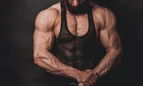 A muscular man with a beard is flexing his arms.