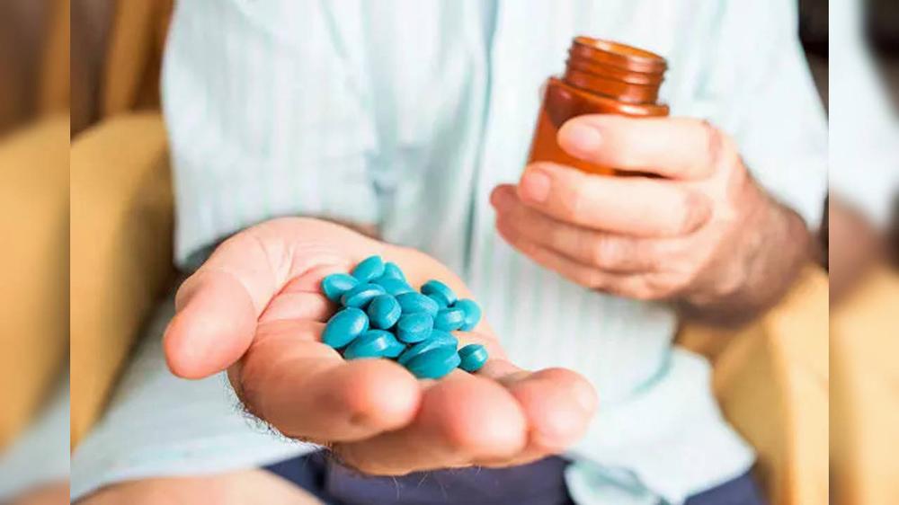 A person is holding a handful of blue pills in the palm of their hand.