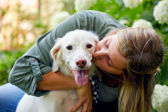 A blonde woman hugs and kisses a large white dog in a backyard.