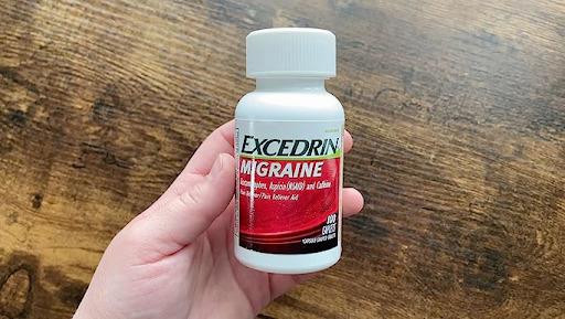 A hand holding a bottle of Excedrin Migraine pain reliever.