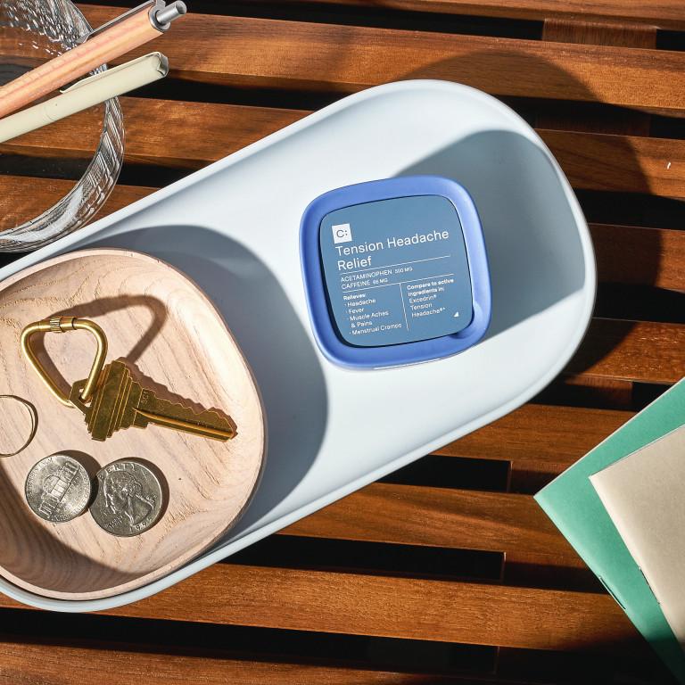 A blue and white box of Tension Headache Relief pills next to a wooden bowl with keys and coins on a table.
