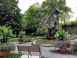 A park with a bench, surrounded by trees, plants and a metal sculpture.