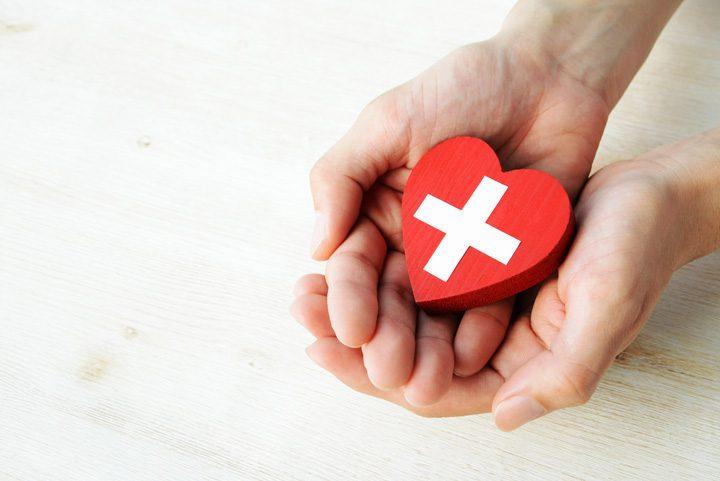 A person is holding a red heart-shaped ornament with a white cross on it.