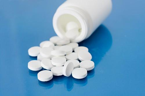 A close-up image of a white pill bottle with white pills spilled out onto a blue surface.