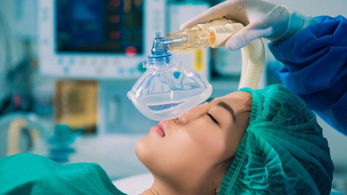 A patient is being put under anesthesia with a mask over her face.