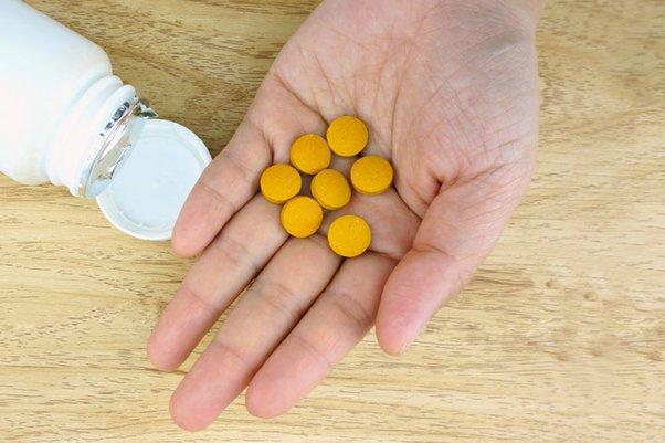 An open bottle of pills next to a hand holding several pills.