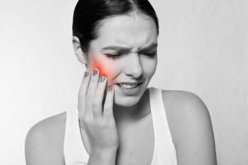 A woman holds her cheek in pain, indicating a toothache.