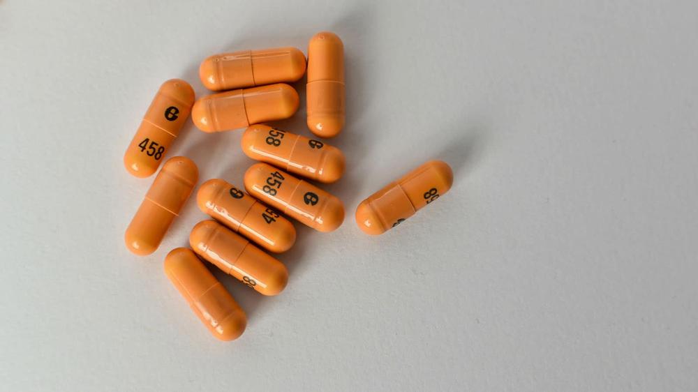 Several orange pills are scattered on a white table.
