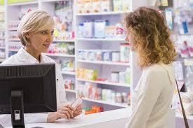 A female pharmacist is talking to a customer while holding a prescription.