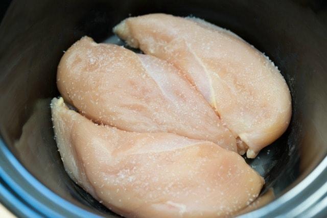 Raw chicken breasts in a slow cooker.