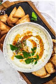 A bowl of homemade tzatziki dip with pita bread and fresh herbs on a wooden board.