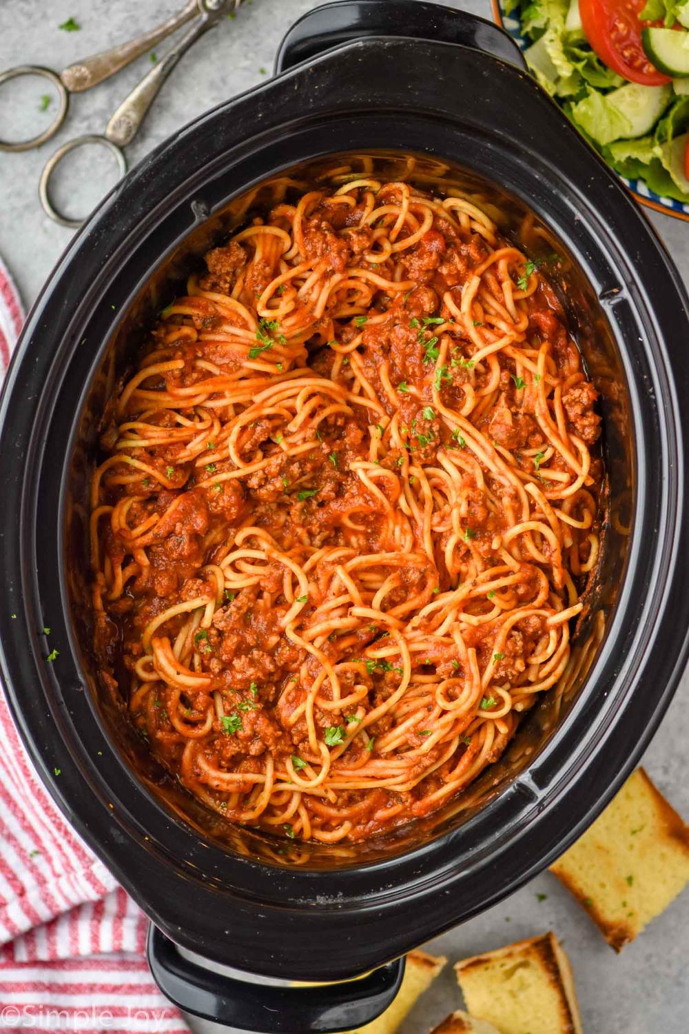 Spaghetti and ground beef in a slow cooker with a side salad and garlic bread.