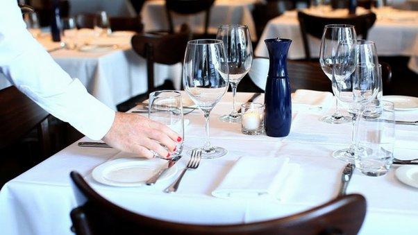 A server sets a glass on a table in a nearly empty restaurant.