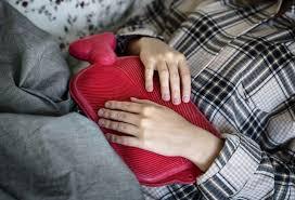 A young woman is holding a hot water bottle to her abdomen.
