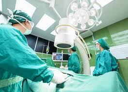 A team of surgeons in green scrubs perform an operation in a modern operating room.