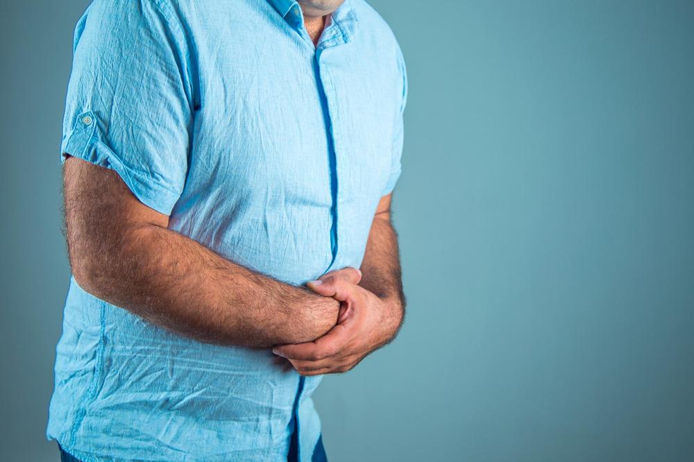 A man in a blue shirt holds his stomach in pain.